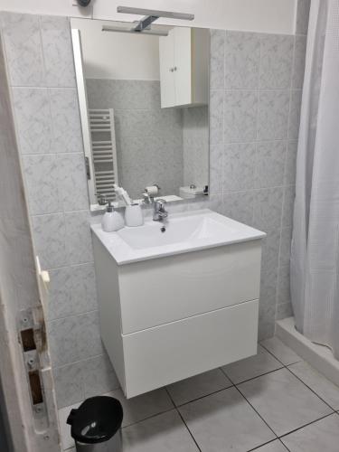 une salle de bain blanche avec un lavabo et un miroir dans l'établissement Location saisonnière, à Agde