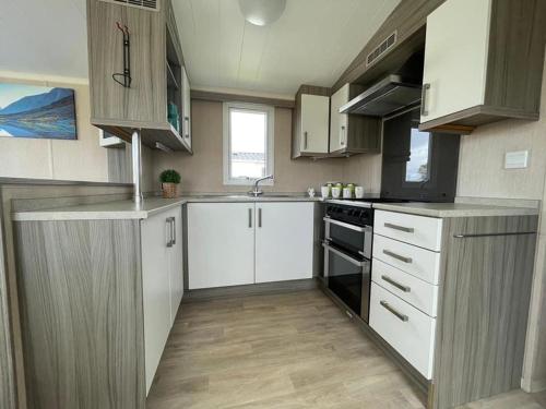 uma cozinha com armários brancos e um forno com placa de fogão em Marine Holiday Park em Rhyl