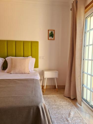 a bedroom with a bed with a green headboard and a window at Homefield Gardens by HnM in Conceição