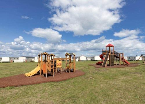 un parque infantil con 2 equipos de juego en un campo en MOONSTONE Lymington en Leysdown-on-Sea