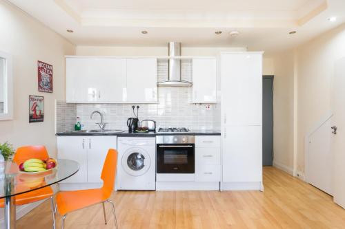 a kitchen with white cabinets and a table with orange chairs at Comfortable Budget Apartment Next To Eurostar International - Kings Cross & Euston Station in London