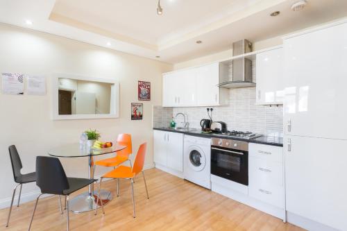 a kitchen with white cabinets and a table and chairs at Comfortable Budget Apartment Next To Eurostar International - Kings Cross & Euston Station in London