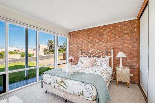 a bedroom with a brick wall and a bed and windows at Beachfront Views at Southern Sands 1 in Port Elliot