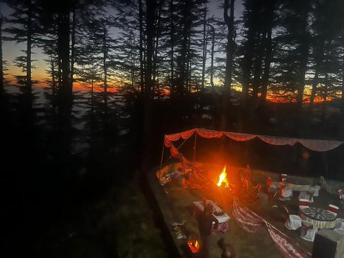 a tent with people sitting around a fire at sunset at Norvin Homes in Shimla