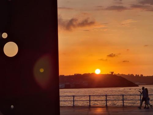 a sunset over the water and a man walking on a pier at 1930 Diecinueve Treinta "Diseño, historia y confort en el centro de Gijón" in Gijón