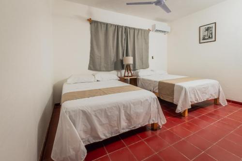 two beds in a room with a red tile floor at Creta Hotel & Suites in Mazatlán