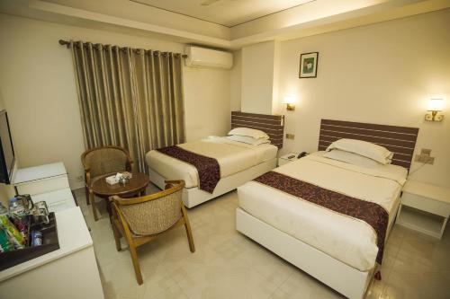 um quarto de hotel com duas camas e uma mesa em Hotel Shuktara Dhaka em Daca