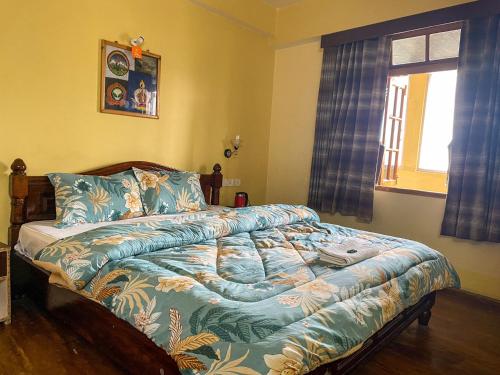 a bedroom with a bed with a blue comforter and a window at King Thai Hotel and Restaurant in Kalimpong