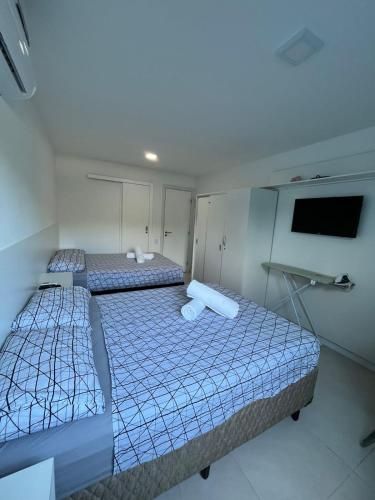 two beds in a small room with a tv at Golden Lake - 1 quarto in Arraial do Cabo
