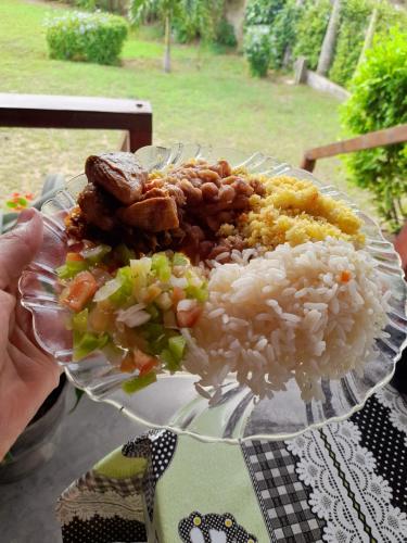 a person holding a plate of food with rice and meat at Pousada Vale Encantado in Serra de São Bento