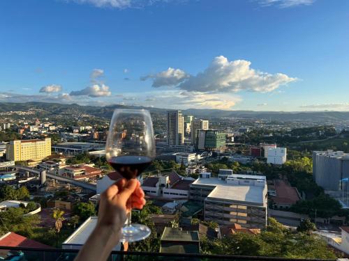 a person holding a glass of wine in front of a city at JF Three Bedroom Apartment in Tegucigalpa