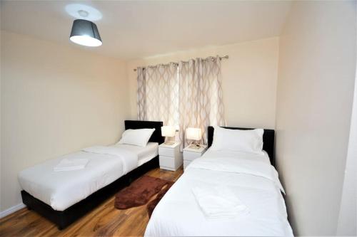 two beds in a room with white walls and wooden floors at Spacious Two-Bedroom Apartment in Dagenham