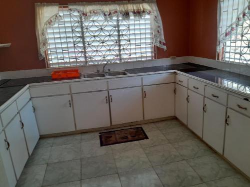 a kitchen with white cabinets and a sink and a window at Villa Chinnor-Kent Ave in Montego Bay