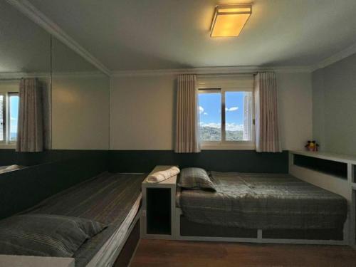 1 dormitorio con 2 camas y 2 ventanas en Apartamento Luxo 3 quartos Gramado próximo ao centro locação de temporada, en Gramado