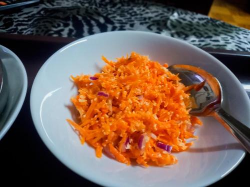 a white plate with carrots and a spoon on it at Ella Happy View Homestay in Ella
