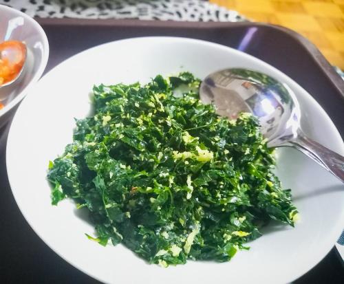 a white bowl of greens with a spoon on a tray at Ella Happy View Homestay in Ella