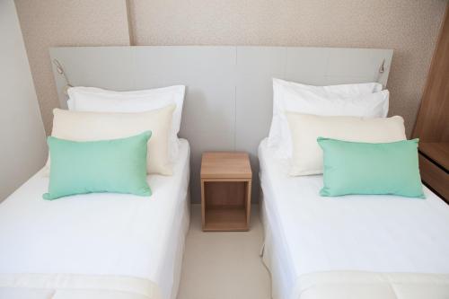 two beds with white and blue pillows and a side table at Intercity Brasilia Led Aguas Claras in Brasilia