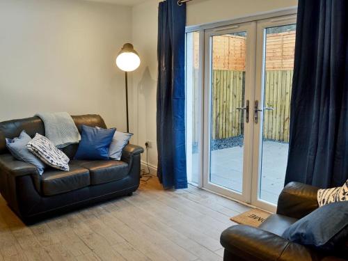 uma sala de estar com um sofá de couro e uma porta de vidro deslizante em Stable Cottage em Stewarton