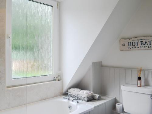 baño con bañera, aseo y ventana en Raglan Cottage, en Ardentinny