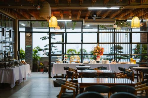 un restaurante con mesas y sillas blancas y ventanas en LARA HOTEL LONG XUYÊN en Long Xuyên
