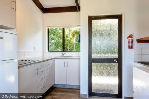 a kitchen with white cabinets and a door with a window at Unit 7 Kaiteri Apartments and Holiday Homes in Kaiteriteri