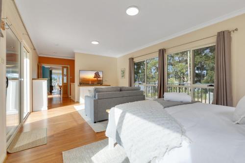 a bedroom with a bed and a couch and windows at Tall Trees- Forest hideaway on Hastings Lagoon in Hastings