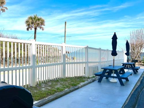 two picnic tables with umbrellas next to a fence at Just Beachy -Ocean View at Symphony Beach Club in Ormond Beach