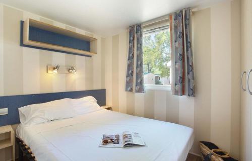 a bedroom with a bed with a book on it at Mobil home 6 ou 8 pers Au camping Le Grau-du-Roi Domaine l'Elysée in Le Grau-du-Roi