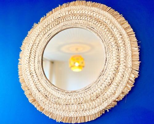 a rattan mirror with a rope frame on a blue wall at Brest - Le Gestin - Appartements - Lumineux - Tout Confort - Fibre Internet in Brest