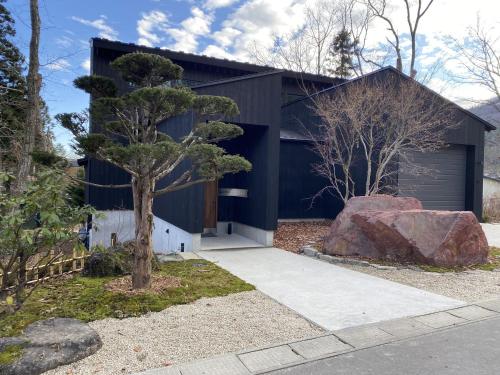 une maison noire avec un arbre et un rocher dans l'établissement NIVIA, à Hakuba