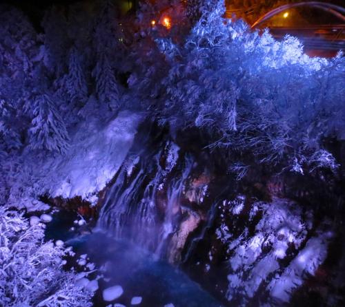 a waterfall covered in snow and trees at night at Biei Shirogane Onsen AONOBI YUYU in Biei