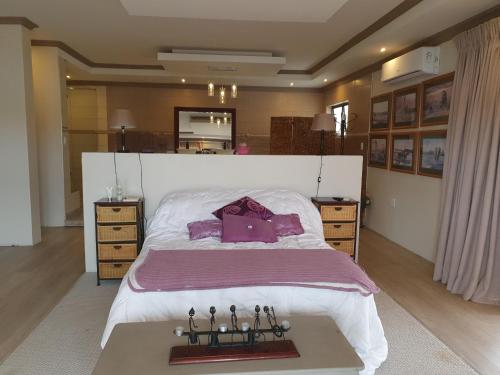 a bedroom with a large white bed with purple pillows at Goggas Nest BNB & Restaurant in Matsapha