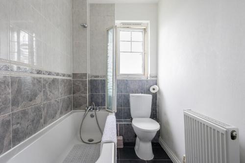 a bathroom with a toilet and a tub with a window at Beautiful Comfortable House in Thamesmead