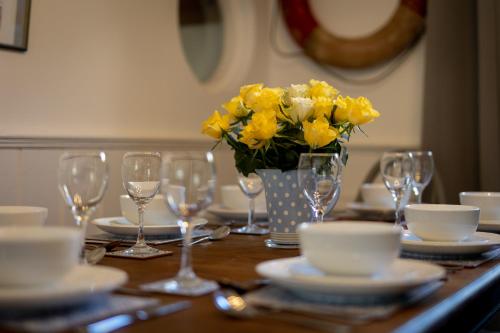 a table with glasses and a vase of yellow flowers at Sunbury Villa - Close to Town and Beaches in Tenby