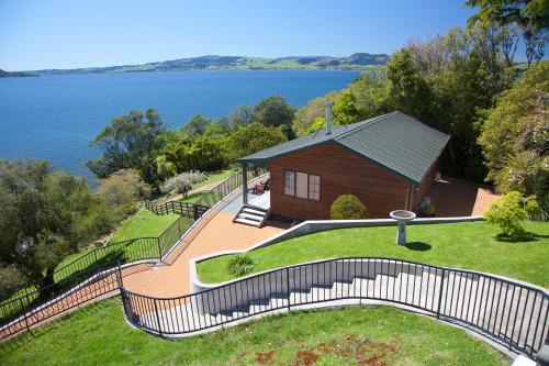 a house with a fence next to the water at On The Point - Lake Rotorua in Rotorua