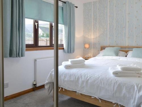 a bedroom with a bed with white sheets and a window at Coiltie Cottage in Drumnadrochit