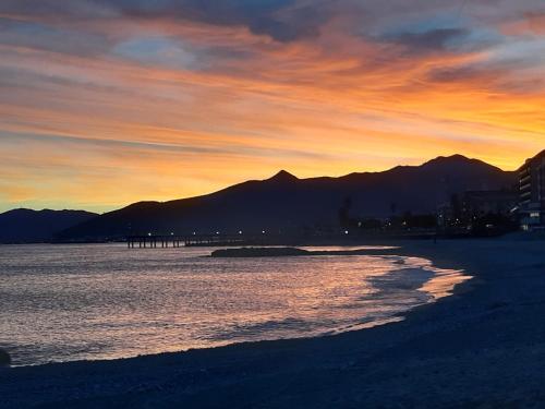 a sunset on a beach with mountains in the background at Bressa de Ma affittacamere, room & breakfast in Pietra Ligure