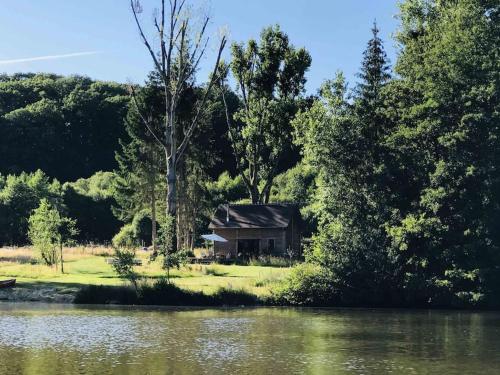 a cabin next to a river with trees at La cabane de l'étang in Feings