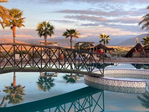 a bridge over a pool with palm trees and mountains at Les Jardins d Amizmiz 6 piscines in Marrakech