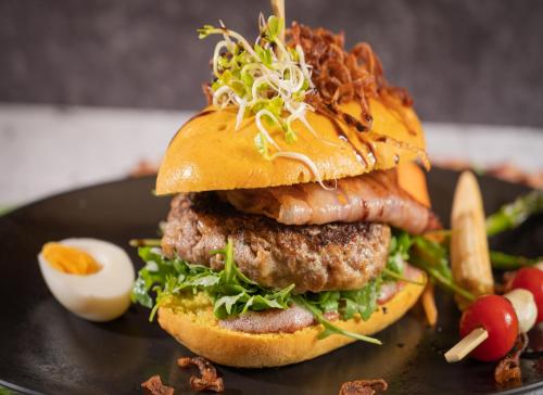 a hamburger on a black plate with an egg and vegetables at Gasthof Rieder Stubn Hotel#Restaurant#Pinseria Lifestyle & Tradition in Ried im Oberinntal