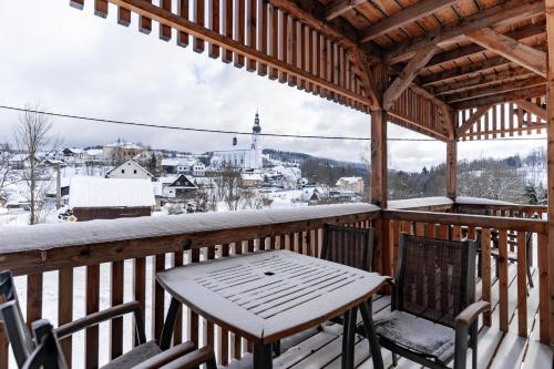 a wooden table and chairs on a porch with a snow covered at Apartmány NONE in Branná