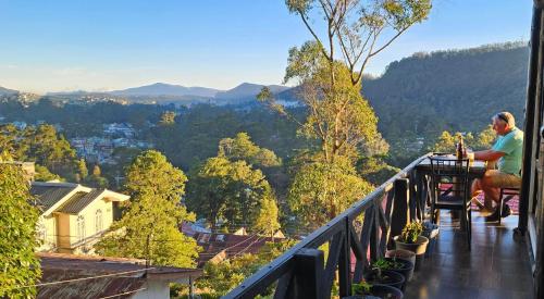a man sitting at a table on a balcony with a view at Chez Allen in Nuwara Eliya