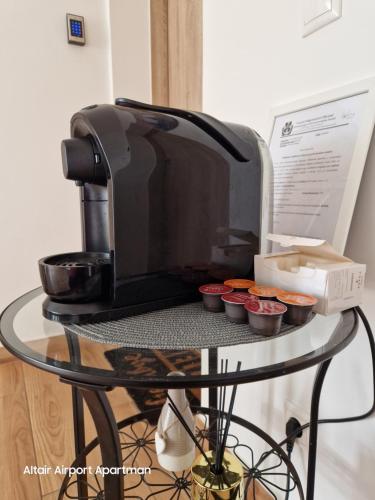 a coffee maker sitting on a glass table with cupcakes at Altair Airport Apartman in Vecsés