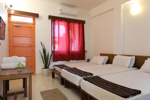 dwa łóżka w pokoju z czerwonym oknem w obiekcie Teles Westend Hotel w mieście Marmagao