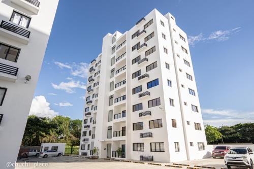 a tall white building with cars parked in a parking lot at Chuchi Place in Santiago de los Caballeros