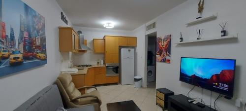 a living room with a kitchen and a tv on a wall at Apartment Amdar Village עם ממ"ד in Eilat