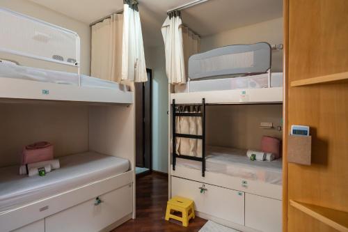 Cette petite chambre comprend des lits superposés blancs et un tabouret jaune. dans l'établissement Hostel B2B SP, à São Paulo