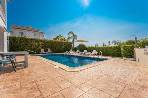 a swimming pool in a yard with chairs and an umbrella at Villa Mespila_ Ayia Napa in Ayia Napa
