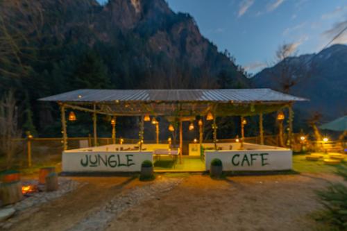 a gazebo with a table and chairs and a mountain at Jungle Hostel by Whoopers in Kasol