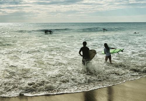 a man and woman walking into the ocean with surfboards at Hotel Tranquilo in Las Peñitas